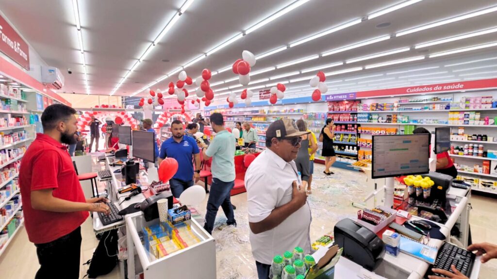 Interior de farmácia com clientes e equipe no balcão durante inauguração, representando acompanhamento de indicadores no primeiro mês
