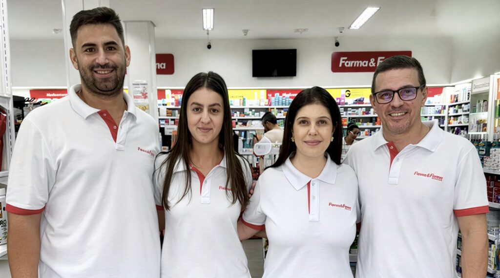 Rafaela, Ailton e seus cônjuges posam sorrindo dentro da Farma e Farma de Fernandópolis, com prateleiras de produtos e comunicação visual da marca ao fundo.