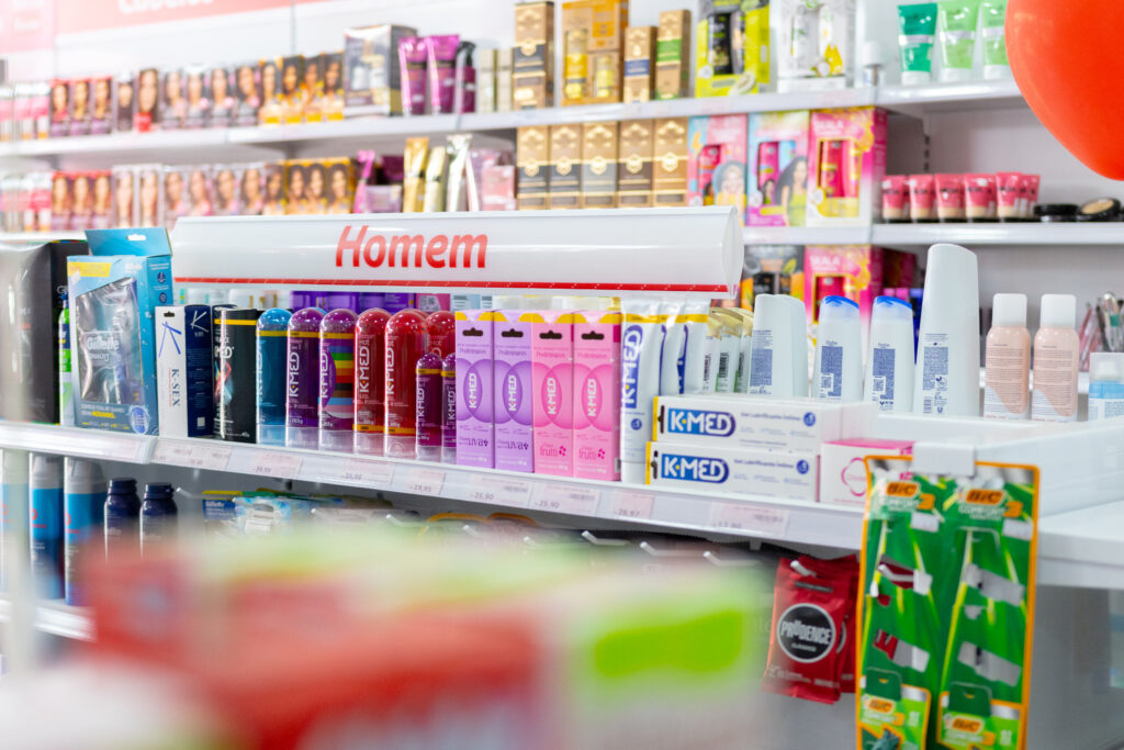 Gôndola “Homem” em farmácia com produtos de cuidados pessoais masculinos, preservativos e itens de higiene organizados por categoria.