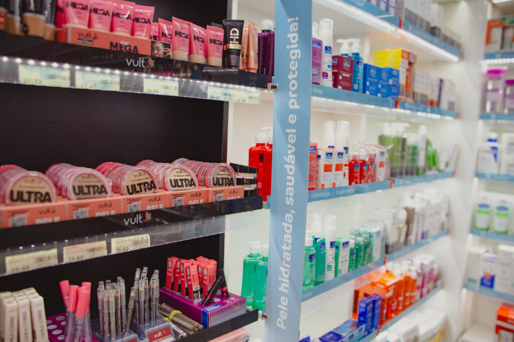 Prateleiras de farmácia com produtos de maquiagem, skincare, proteção solar, hidratação e cuidados pessoais em exposição organizada.