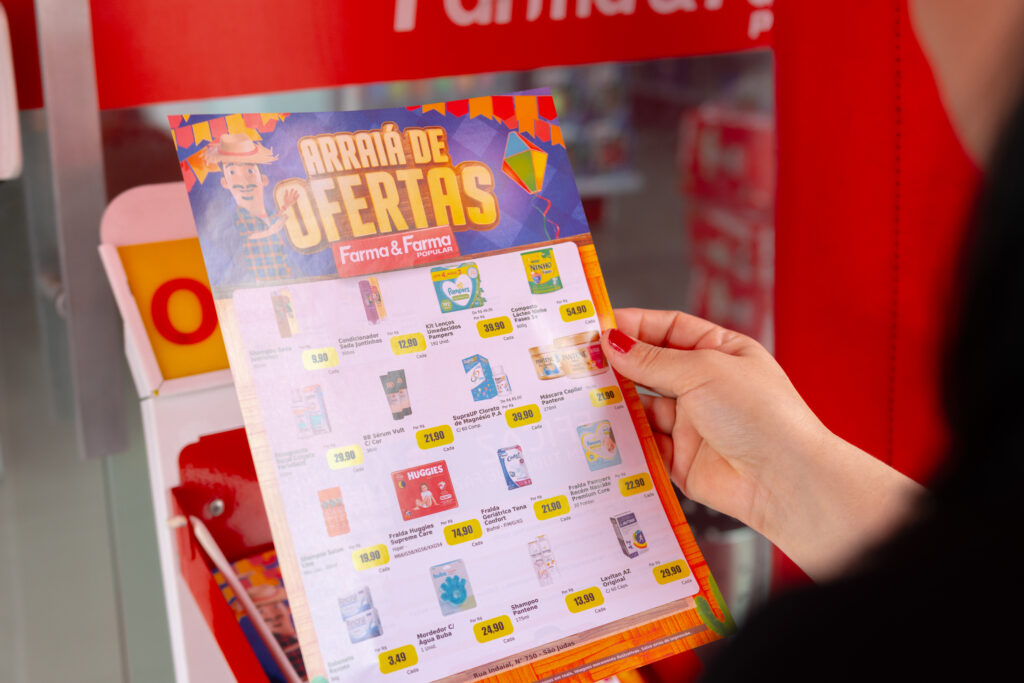 Mão segurando encarte promocional de ofertas da Farma e Farma dentro da farmácia.